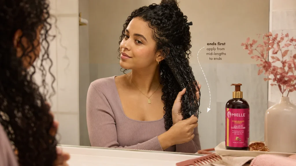 applying Mielle leave-in conditioner to wet curly hair from mid lengths to ends