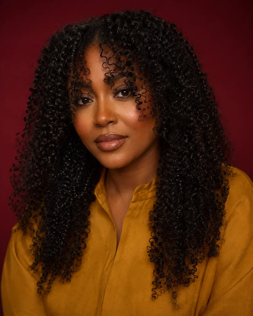 Long tight curls with dry curtain bangs settling near the eyes and cheekbones.
